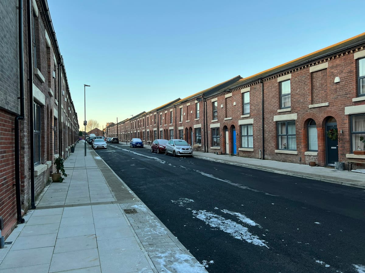 A street lined with brick terraced houses and parked cars